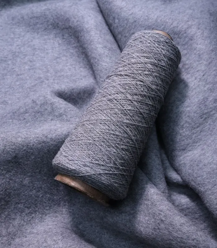 Grey spool of wool yarn resting on a piece of grey woolen fabric.